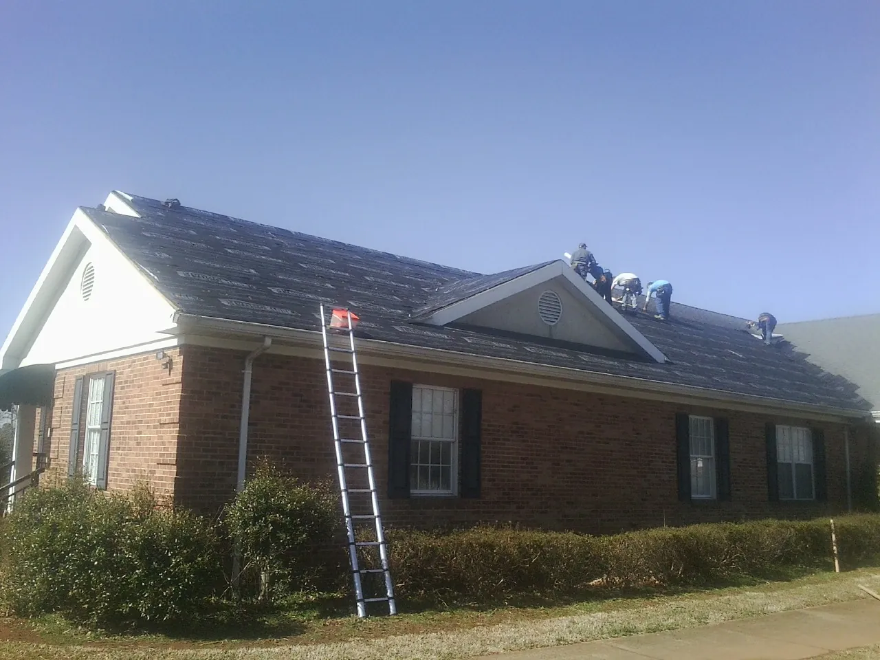 Crew tearing shingles off a brick ranch roof with a ladder set — Emergency Roof Repair work by our crew in Hortonville