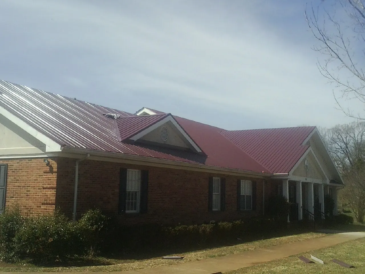 Red metal roof with gabled entries on a long brick building, from a Hail Damage Roof Repair job in Hortonville