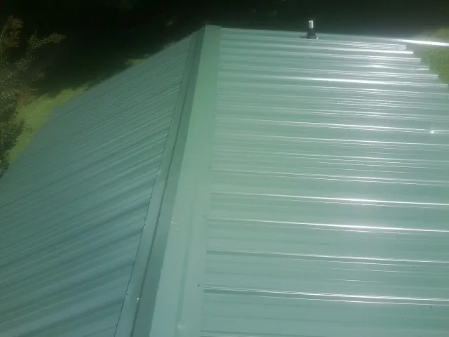 New green metal panels meeting at the ridge of a roof — Flat Roof Repair work by our crew in Hortonville