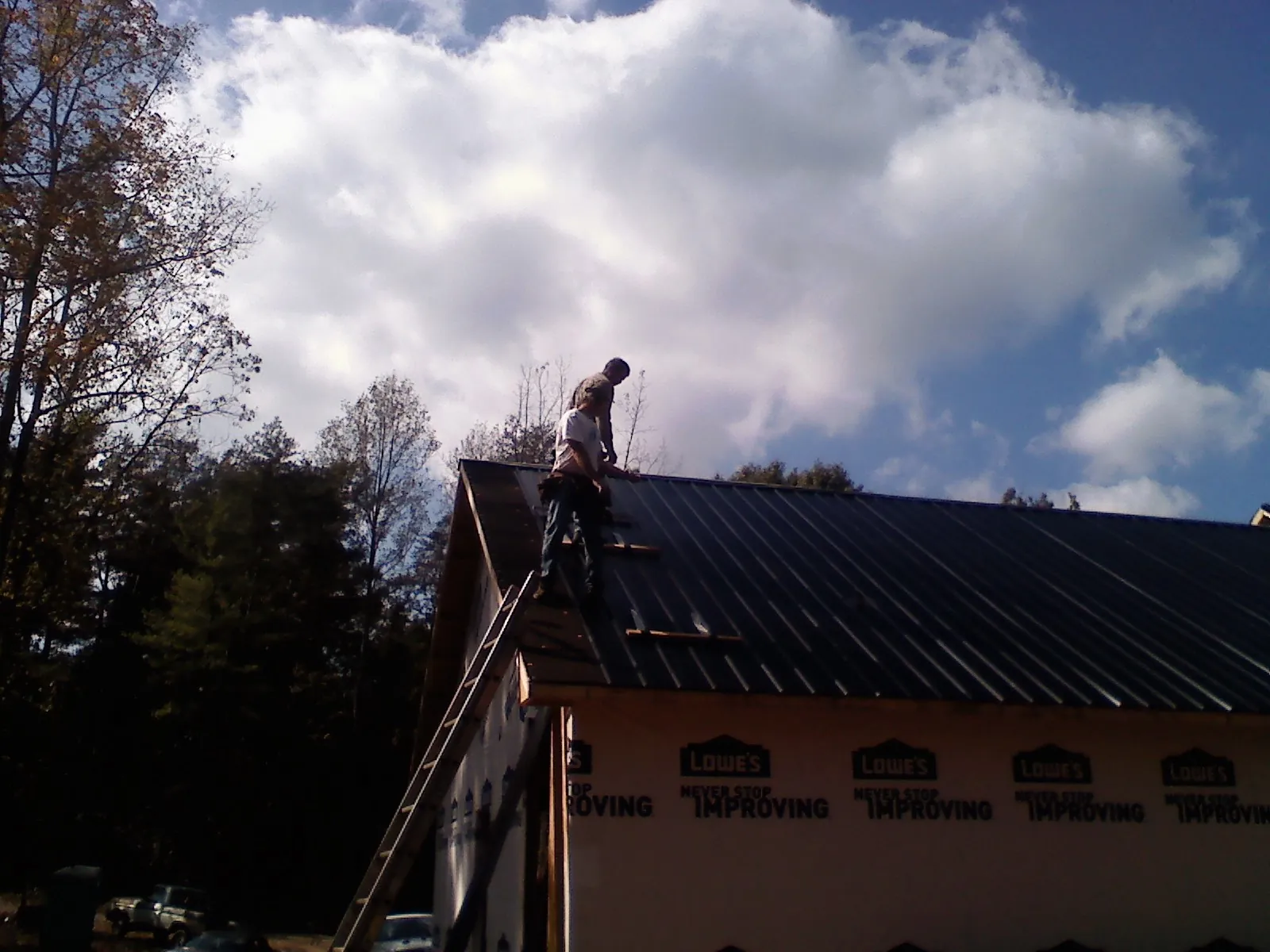 Roofer fastening dark metal panels high against a cloudy sky, from a Roof Inspection job in Hortonville