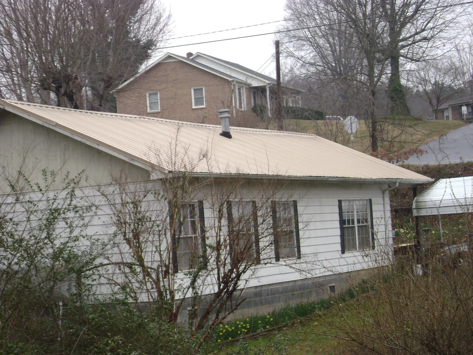 Tan metal roof on a white sided house set into a hillside — Commercial Roofing by Roofing Brothers in Hortonville
